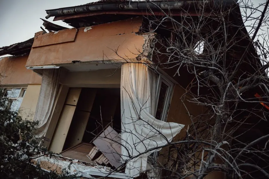 Storm-damaged house with a broken balcony wall and torn curtains